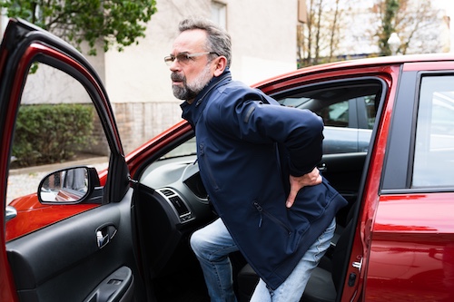 Man experiencing back pain while getting out of a red car, illustrating the impact of spinal cord injuries from car accidents.