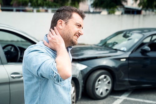 Man with neck pain after car accident, standing near damaged vehicles, illustrating the impact of traffic collisions on personal injury claims.