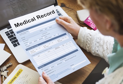 Person holding a medical record form while sitting at a desk with a laptop, emphasizing the importance of obtaining and managing client medical records in car accident cases.