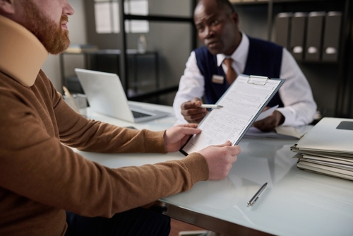 Person with neck brace discussing paperwork with a lawyer in an office setting, emphasizing legal support for motorcycle accident claims in Wilmington, NC.