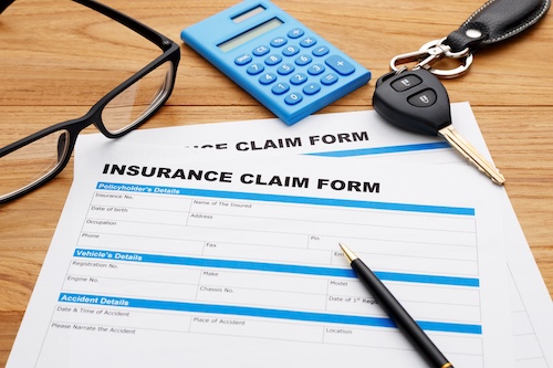 Insurance claim form with details for car accidents, calculator, car keys, and glasses on wooden surface, relevant to legal claims for soft tissue injuries.