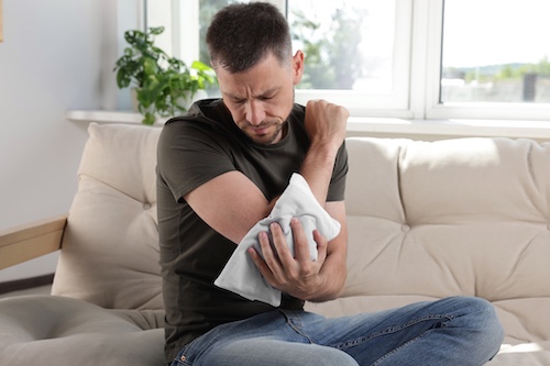 Man sitting on a couch holding an ice pack to his shoulder, illustrating soft tissue injuries related to car accidents.