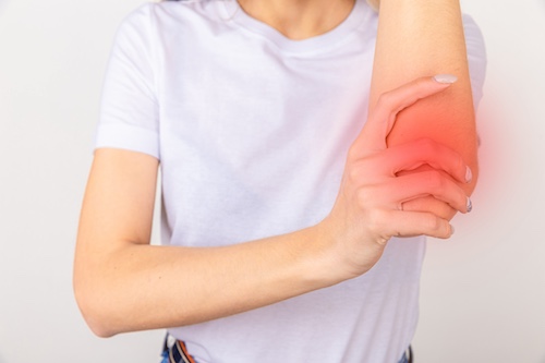 Woman holding her elbow with visible redness, indicating pain from a soft tissue injury, relevant to car accident claims and legal representation for injury compensation.