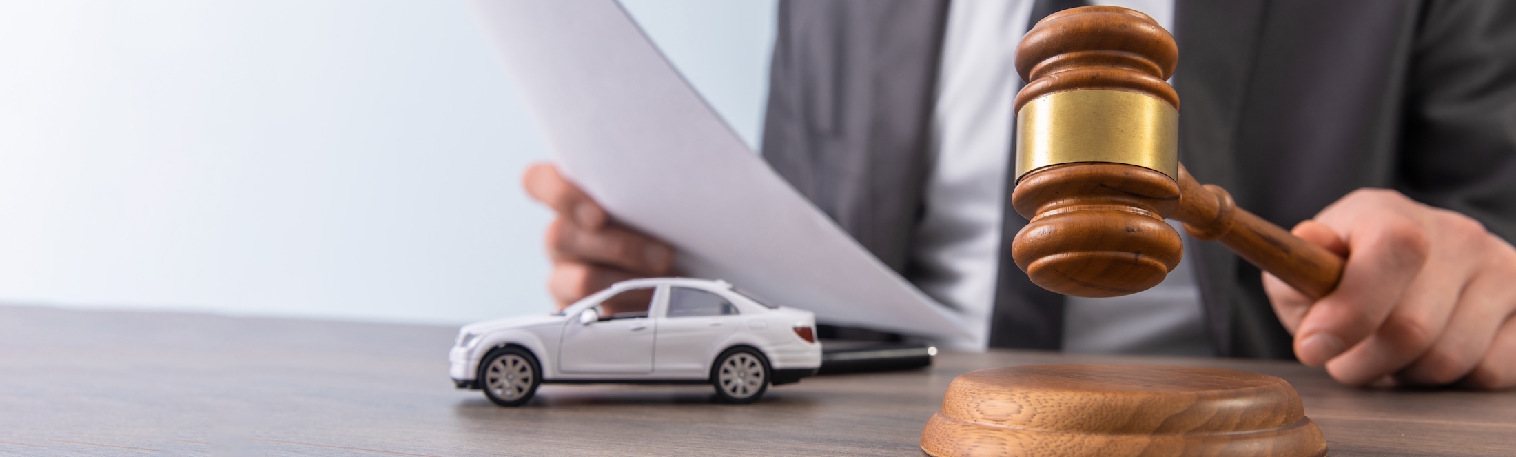 A judge in a dark robe holding a wooden gavel on a sound block beside a white toy sedan and legal papers, representing a car crash lawyer reviewing case details.