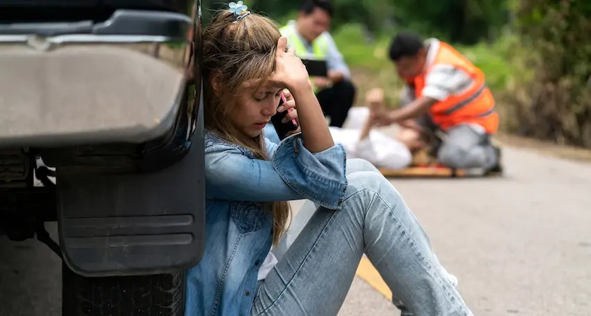 A distressed woman on the phone at an accident scene while emergency responders assist an injured person is in need of car accident attorney representation from North Carolina Car Accident Lawyers.