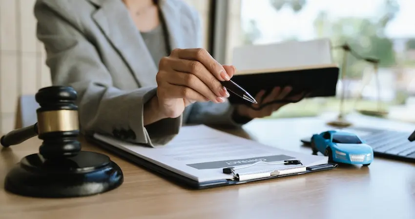 A car accident attorney is reviewing legal case files with a gavel and toy vehicle on the desk for claim preparation at North Carolina Car Accident Lawyers.