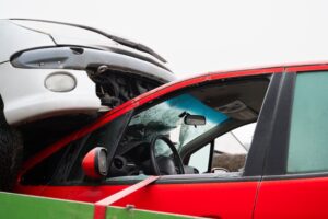 A silver car is rammed on top of a red vehicle with a shattered windshield in a catastrophic overlap collision representing the type of high-speed car accident that causes life-altering injuries and extensive property damage in North Carolina.