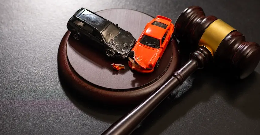 Two damaged toy cars staged in a head-on collision rest on top of a wooden judge's gavel sound block beside a brown and gold gavel symbolizing the legal process of pursuing justice and compensation following a car accident at North Carolina Car Accident Lawyers in North Carolina.