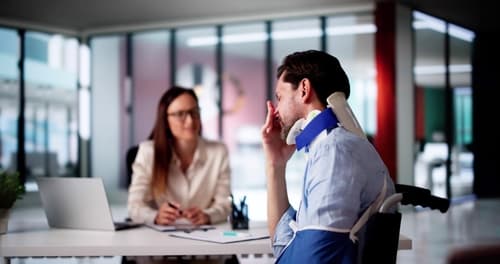A man in a neck brace and arm sling talking to a personal injury lawyer.